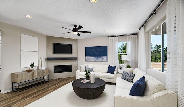 living room featuring a textured ceiling, a large fireplace, dark wood-type flooring, and ceiling fan