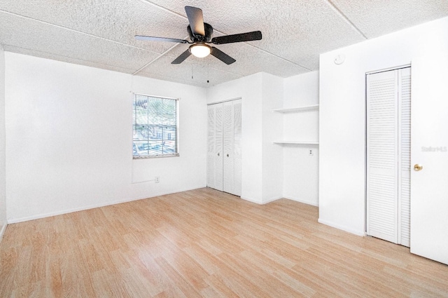 unfurnished bedroom featuring two closets, light hardwood / wood-style floors, and ceiling fan