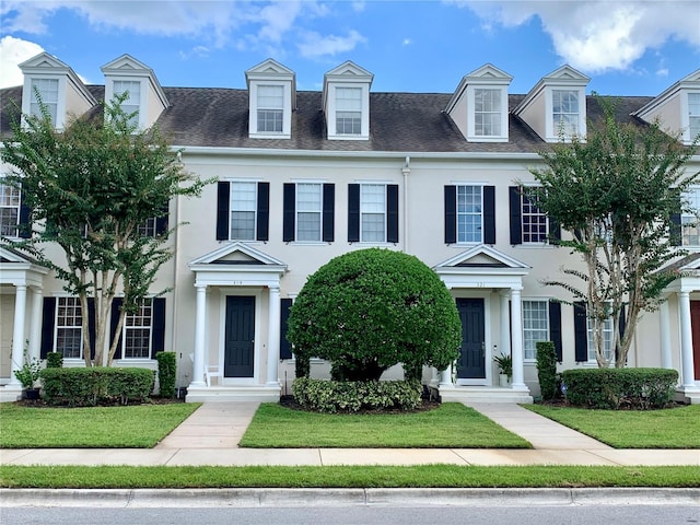 view of front facade featuring roof with shingles, a front lawn, and stucco siding