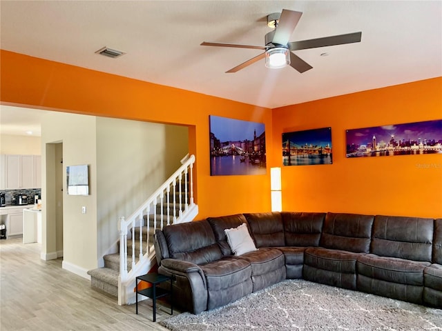 living room with visible vents, baseboards, a ceiling fan, stairway, and light wood-style floors