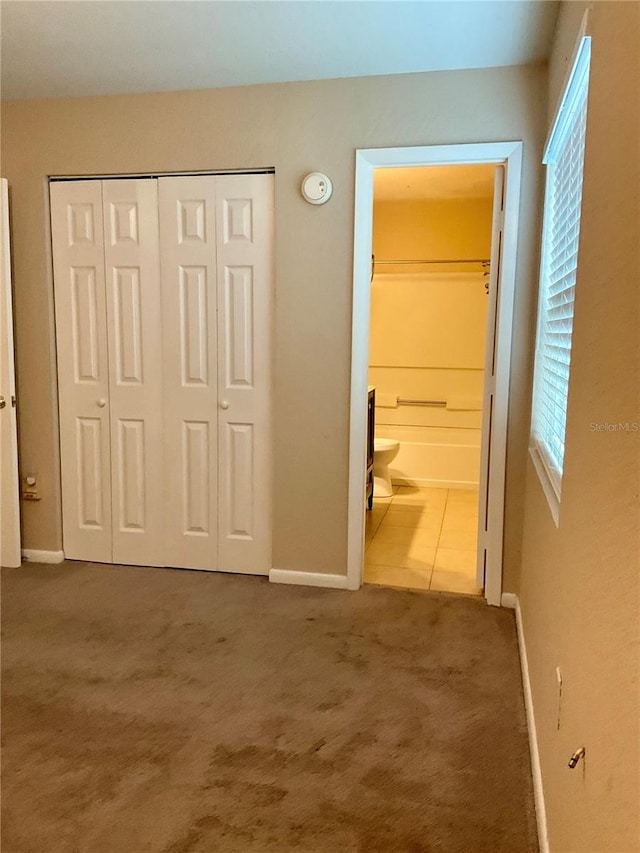 unfurnished bedroom featuring a closet, ensuite bath, and carpet