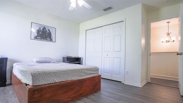 bedroom with a textured ceiling, ceiling fan with notable chandelier, dark wood-type flooring, and a closet