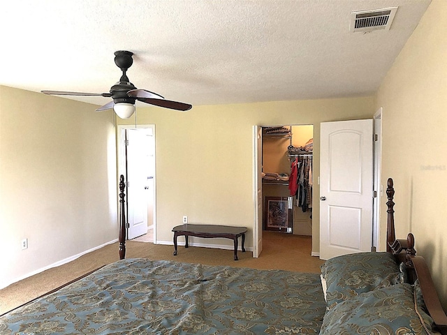 bedroom featuring ceiling fan, a textured ceiling, a closet, a walk in closet, and light colored carpet