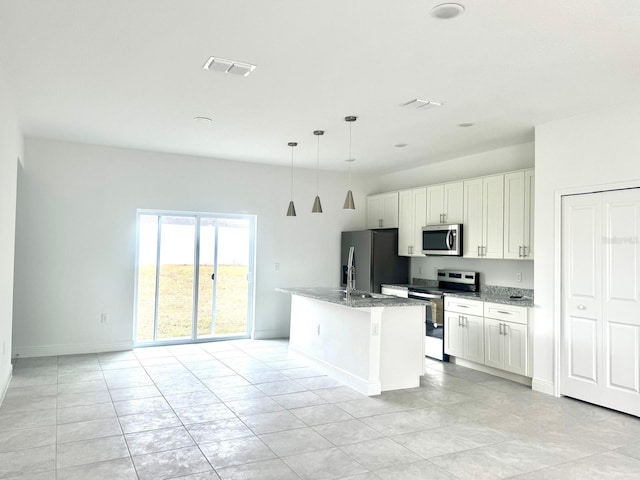 kitchen featuring white cabinets, appliances with stainless steel finishes, decorative light fixtures, light stone counters, and a center island with sink