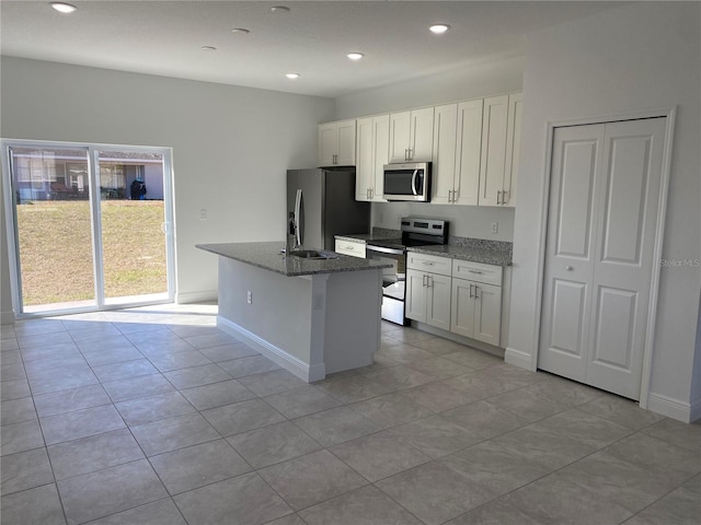 kitchen featuring a kitchen island with sink, white cabinetry, dark stone counters, and appliances with stainless steel finishes