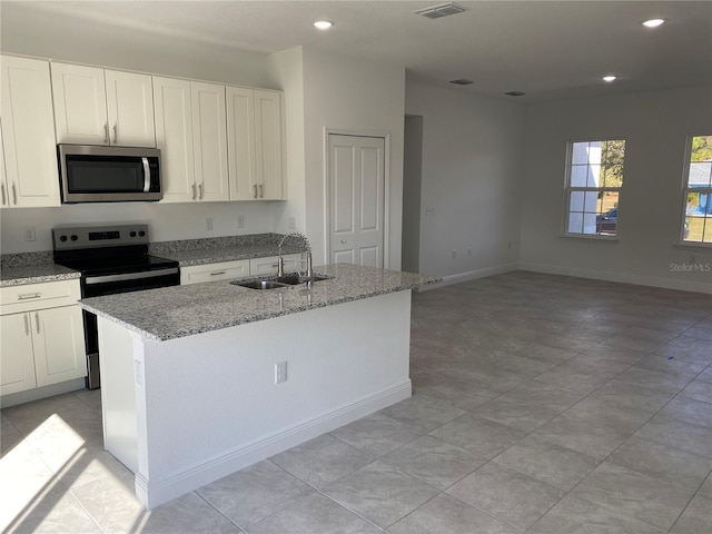 kitchen featuring appliances with stainless steel finishes, sink, white cabinets, light stone counters, and a kitchen island with sink