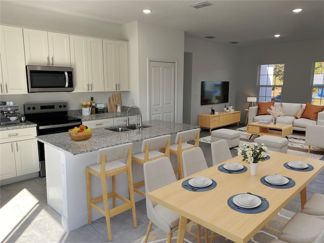 kitchen featuring appliances with stainless steel finishes, sink, an island with sink, light stone counters, and light tile patterned flooring