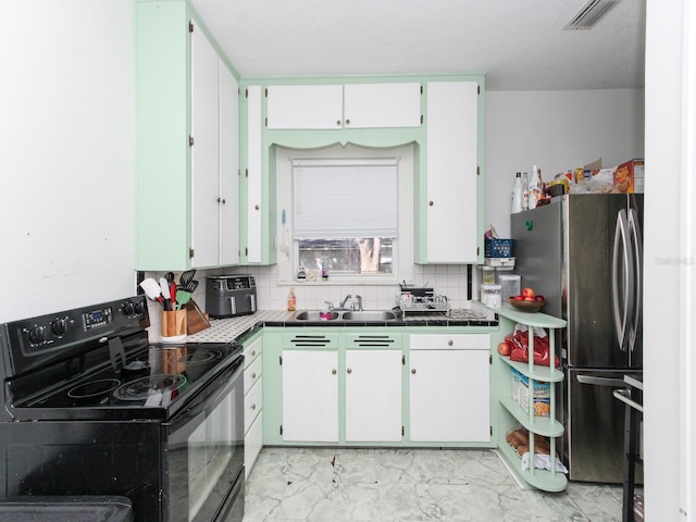 kitchen with black electric range, backsplash, white cabinetry, and stainless steel refrigerator