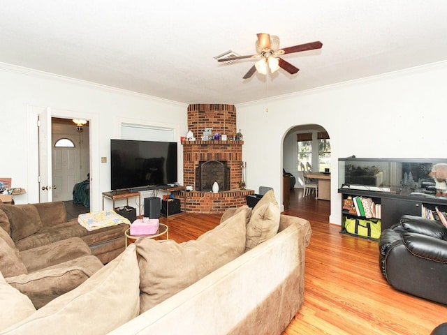 living room with light hardwood / wood-style flooring, ceiling fan, a brick fireplace, and crown molding