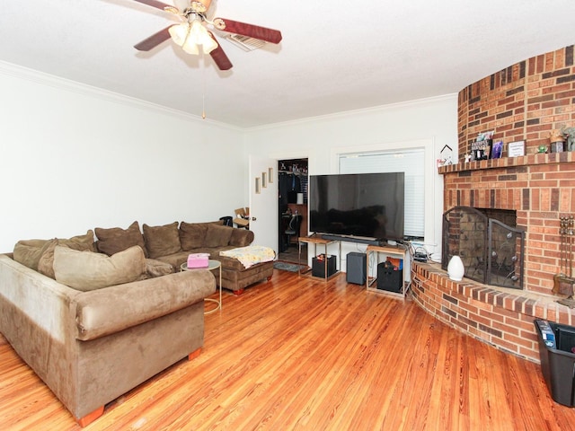 living room featuring crown molding, wood-type flooring, a fireplace, and ceiling fan