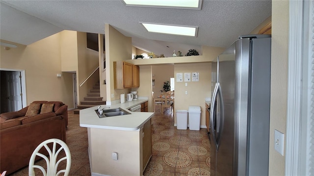 kitchen featuring lofted ceiling, stainless steel fridge, sink, kitchen peninsula, and dark tile patterned floors