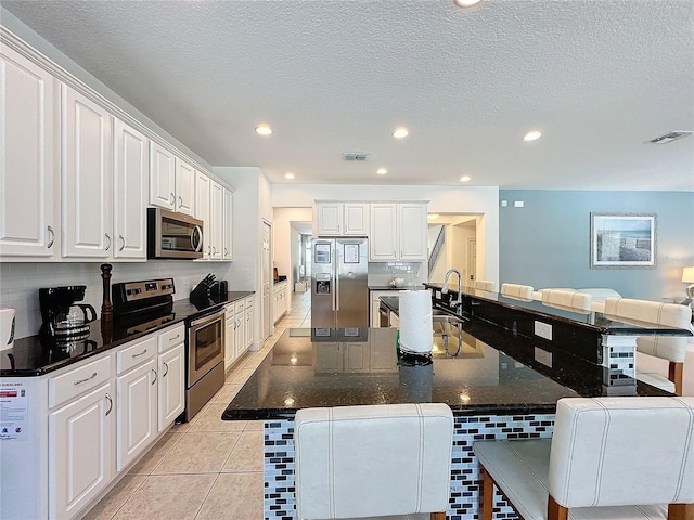 kitchen with white cabinetry, a kitchen bar, stainless steel appliances, and light tile patterned floors