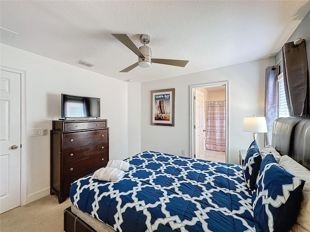 bedroom with a textured ceiling, connected bathroom, light colored carpet, and ceiling fan