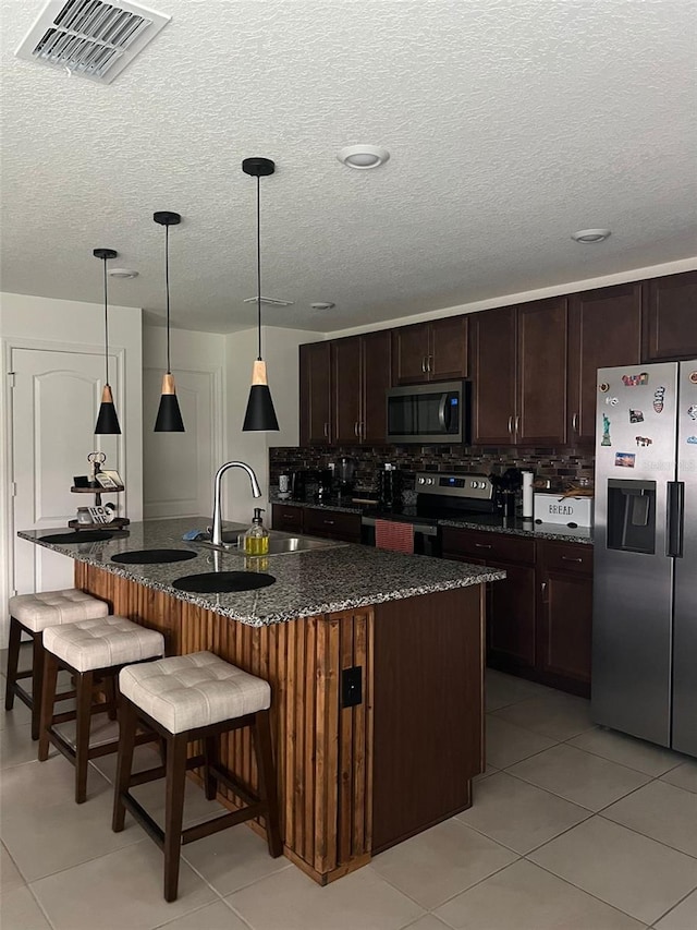 kitchen featuring appliances with stainless steel finishes, a kitchen island with sink, dark stone counters, and sink