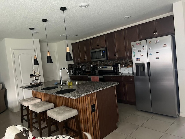 kitchen featuring a center island with sink, sink, hanging light fixtures, light tile patterned flooring, and stainless steel appliances