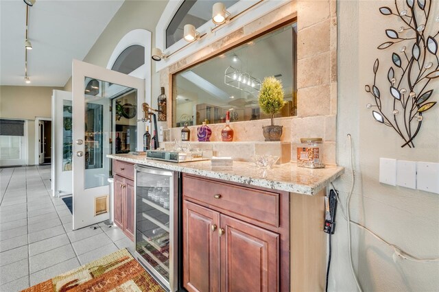 kitchen featuring brown cabinets, rail lighting, light tile patterned flooring, light stone countertops, and beverage cooler