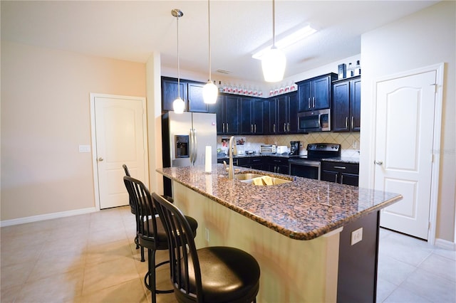 kitchen featuring stainless steel appliances, a center island with sink, dark stone counters, a kitchen bar, and backsplash