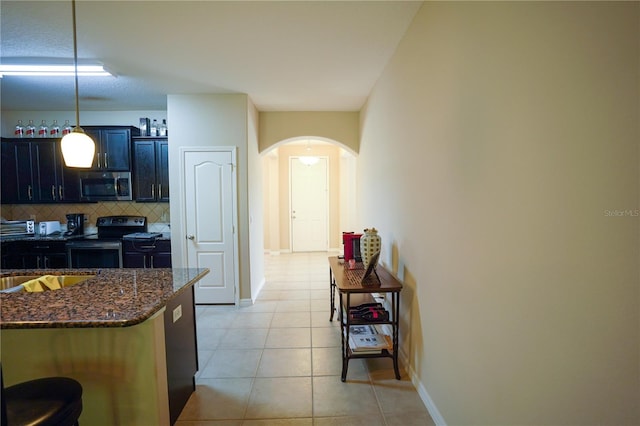 kitchen featuring black electric range, decorative backsplash, hanging light fixtures, a breakfast bar area, and dark stone countertops