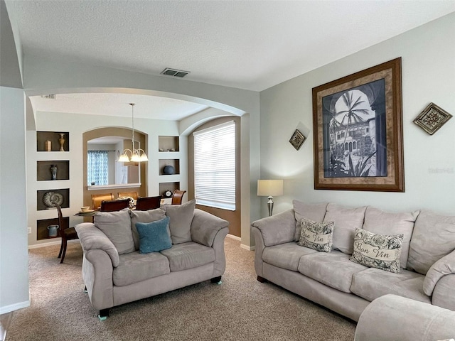 carpeted living room featuring built in shelves, a textured ceiling, and a chandelier