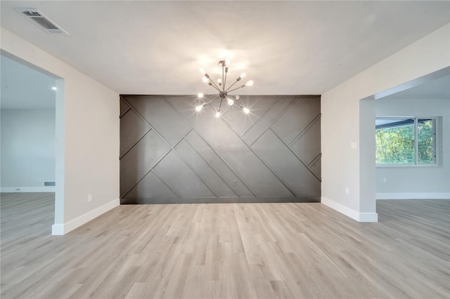 empty room with light wood-type flooring and an inviting chandelier