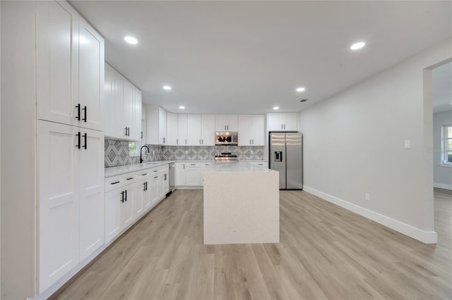 kitchen with white cabinets, sink, a kitchen island, light hardwood / wood-style flooring, and stainless steel appliances