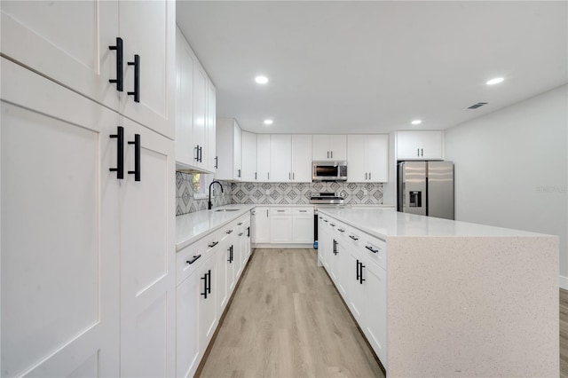 kitchen featuring white cabinets, sink, a kitchen island, appliances with stainless steel finishes, and light wood-type flooring