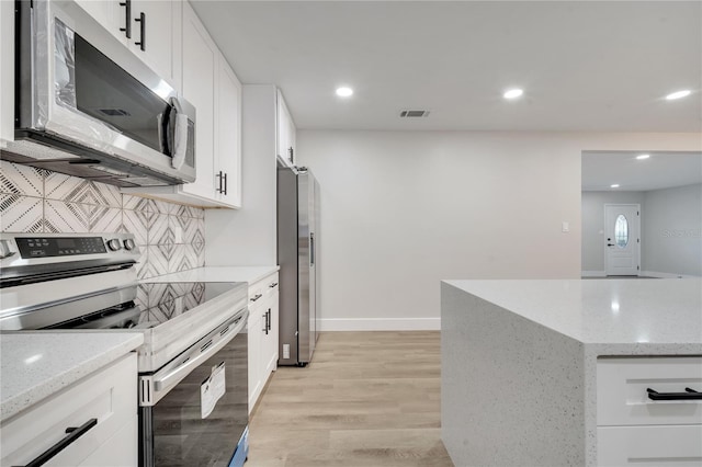 kitchen with appliances with stainless steel finishes, light stone counters, white cabinets, backsplash, and light wood-type flooring