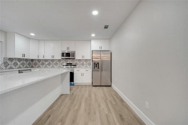 kitchen featuring appliances with stainless steel finishes, light stone counters, tasteful backsplash, white cabinets, and light hardwood / wood-style flooring