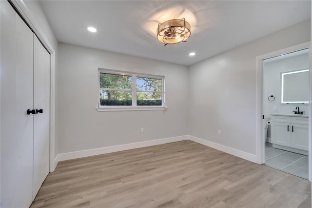 unfurnished bedroom with ensuite bathroom, a closet, sink, and light hardwood / wood-style floors