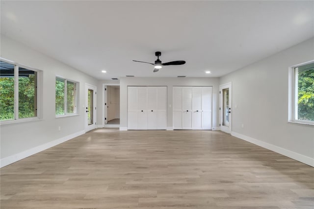 unfurnished bedroom with ceiling fan, two closets, light hardwood / wood-style floors, and multiple windows