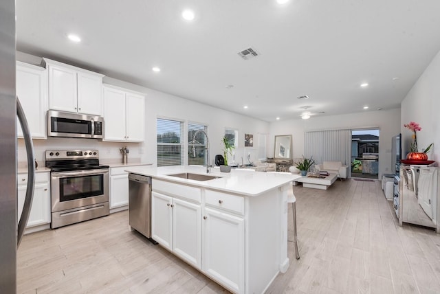 kitchen with light hardwood / wood-style floors, sink, an island with sink, white cabinetry, and appliances with stainless steel finishes