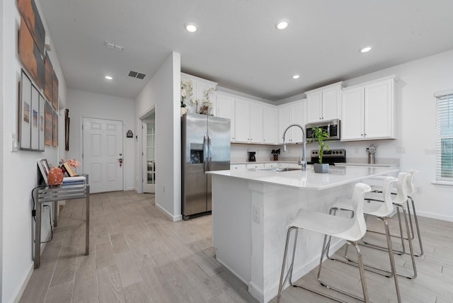 kitchen with a kitchen island with sink, light hardwood / wood-style flooring, white cabinetry, appliances with stainless steel finishes, and a kitchen breakfast bar