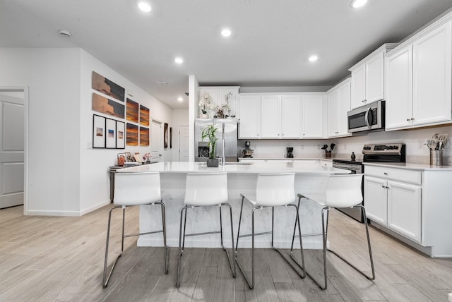 kitchen featuring an island with sink, white cabinets, appliances with stainless steel finishes, and light hardwood / wood-style flooring