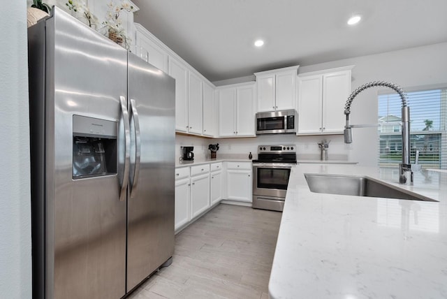 kitchen with light stone counters, sink, light hardwood / wood-style flooring, white cabinetry, and appliances with stainless steel finishes