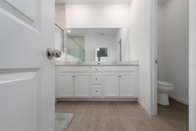 bathroom featuring hardwood / wood-style flooring, walk in shower, vanity, and toilet