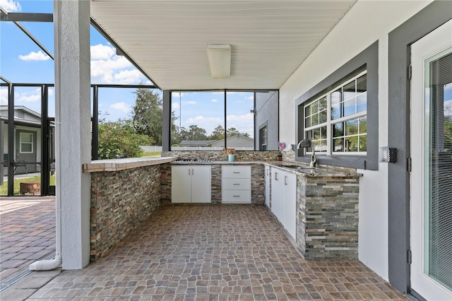 view of patio / terrace featuring a lanai, sink, and an outdoor kitchen