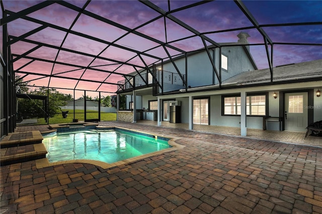 pool at dusk featuring a patio, area for grilling, a lanai, and an in ground hot tub