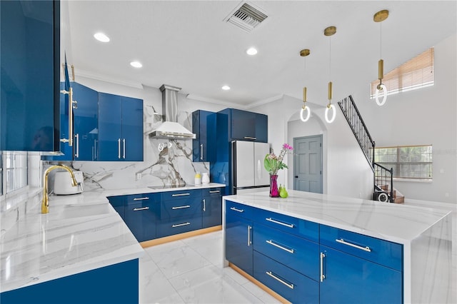 kitchen featuring hanging light fixtures, a kitchen island, wall chimney exhaust hood, light stone counters, and white refrigerator