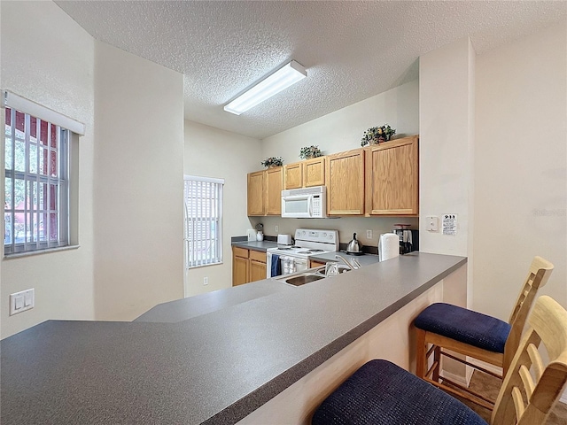 kitchen featuring plenty of natural light, white appliances, a textured ceiling, and kitchen peninsula