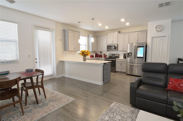 kitchen with kitchen peninsula, stainless steel appliances, decorative light fixtures, decorative backsplash, and dark hardwood / wood-style floors