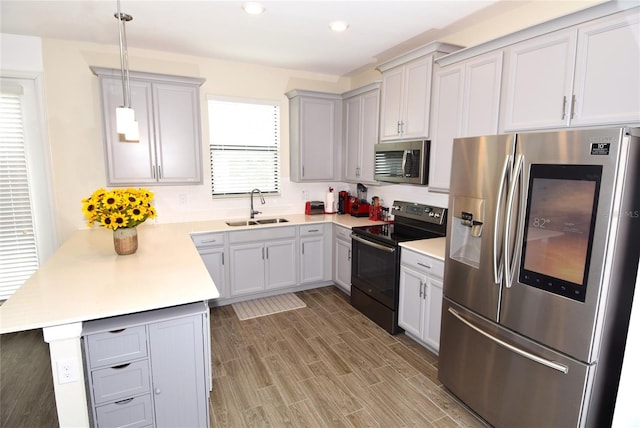 kitchen with kitchen peninsula, appliances with stainless steel finishes, wood-type flooring, pendant lighting, and sink