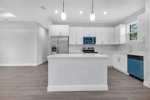 kitchen with hardwood / wood-style floors, a center island, stainless steel appliances, pendant lighting, and white cabinetry