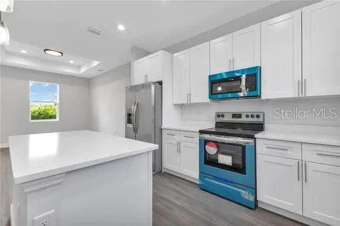 kitchen with dark wood-type flooring, appliances with stainless steel finishes, and white cabinetry