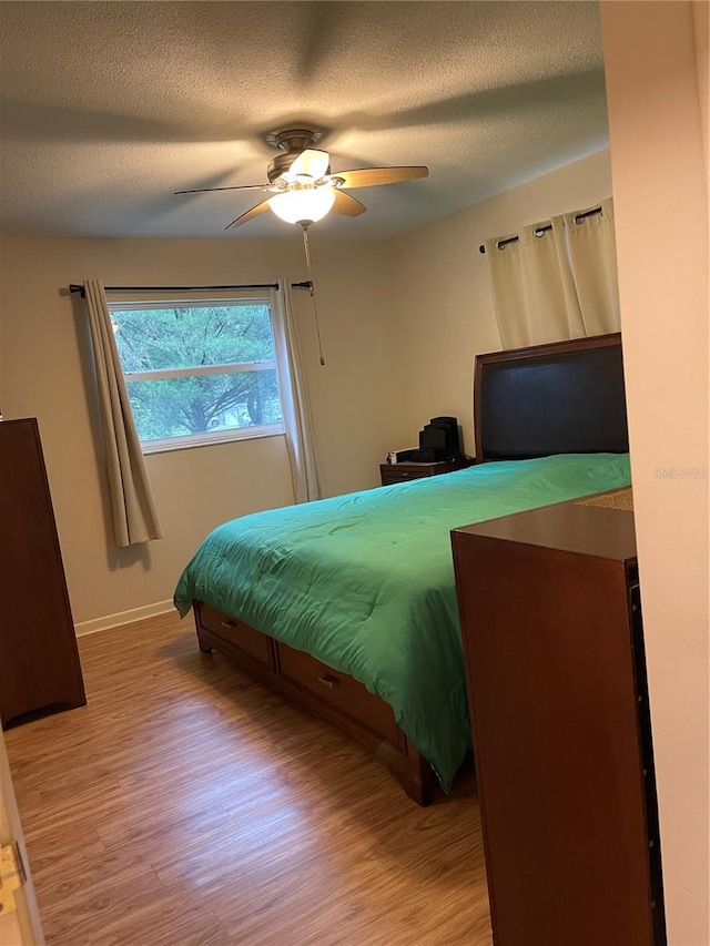 bedroom with light hardwood / wood-style floors, a textured ceiling, and ceiling fan