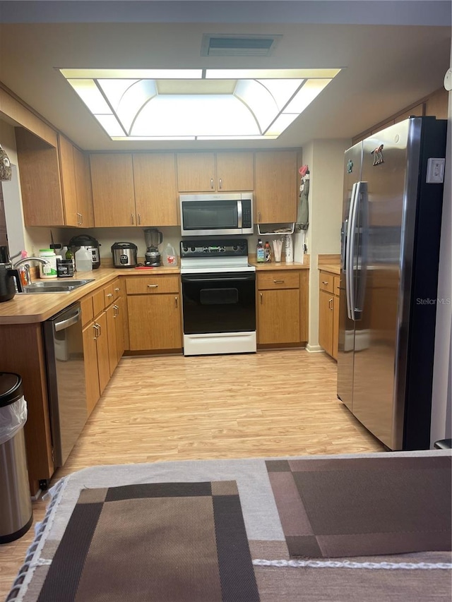 kitchen with appliances with stainless steel finishes, sink, and light hardwood / wood-style flooring