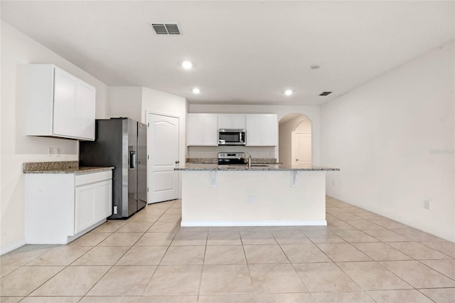 kitchen with a center island with sink, light stone countertops, white cabinetry, and stainless steel appliances