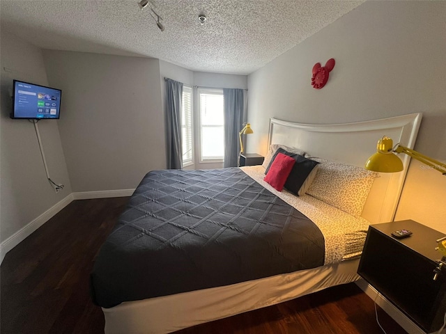 bedroom featuring a textured ceiling, track lighting, and dark hardwood / wood-style flooring