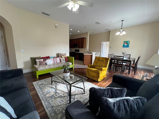 living room with ceiling fan with notable chandelier and dark hardwood / wood-style flooring