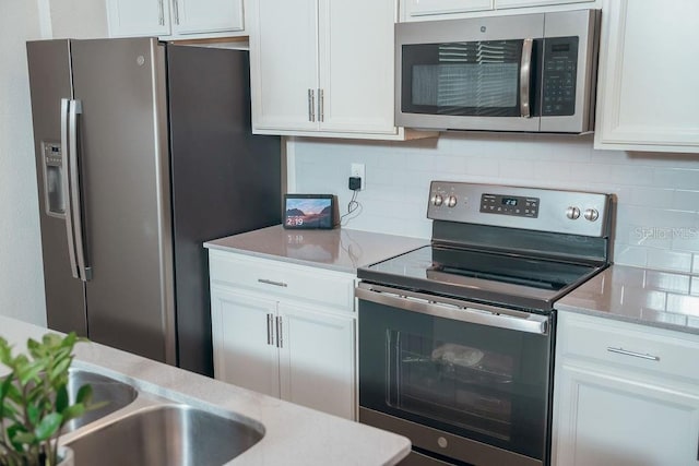 kitchen featuring white cabinetry, light stone countertops, sink, stainless steel appliances, and backsplash