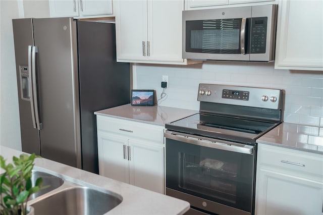 kitchen with sink, stainless steel appliances, light stone counters, decorative backsplash, and white cabinets